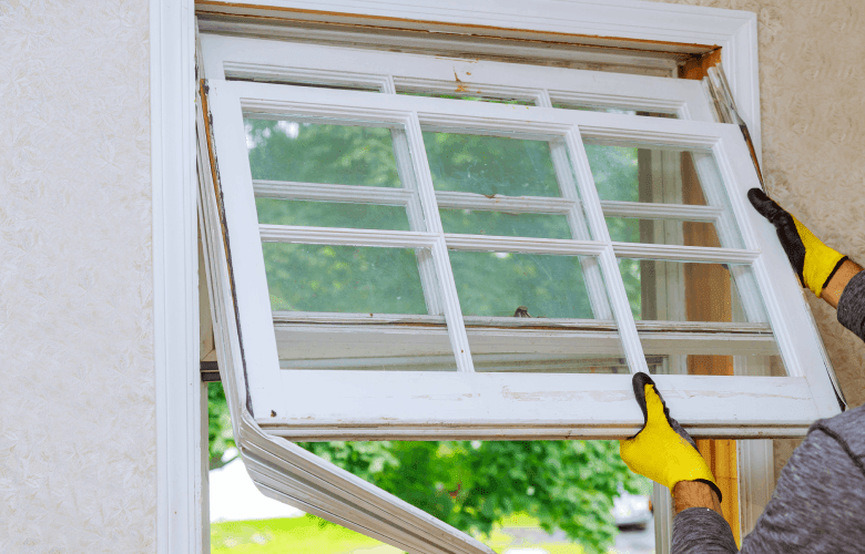 Een bouwvakker met gele handschoenen vervangt een wit raam voor een renovatie.