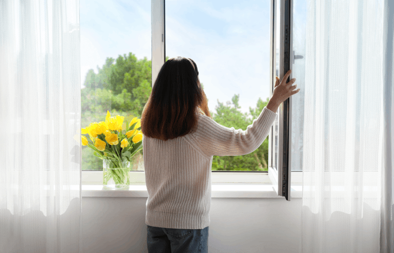 Een jonge vrouw opent witte ramen van fabrikant Deceuninck. Er staan gele tulpen op de vensterbank.