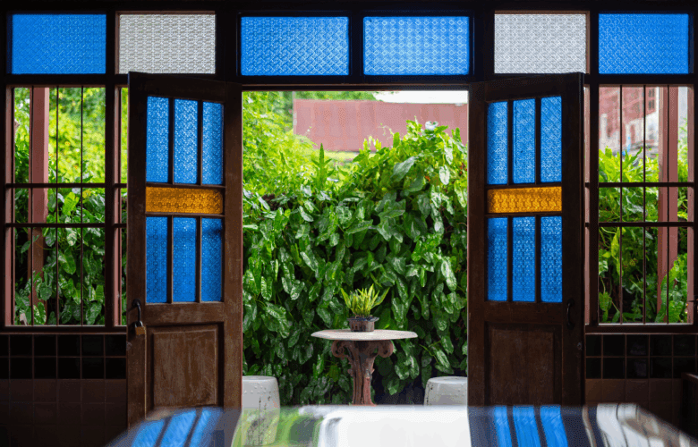 Een houten deur met blauw glas-in-lood en uitzicht op een grote struik.