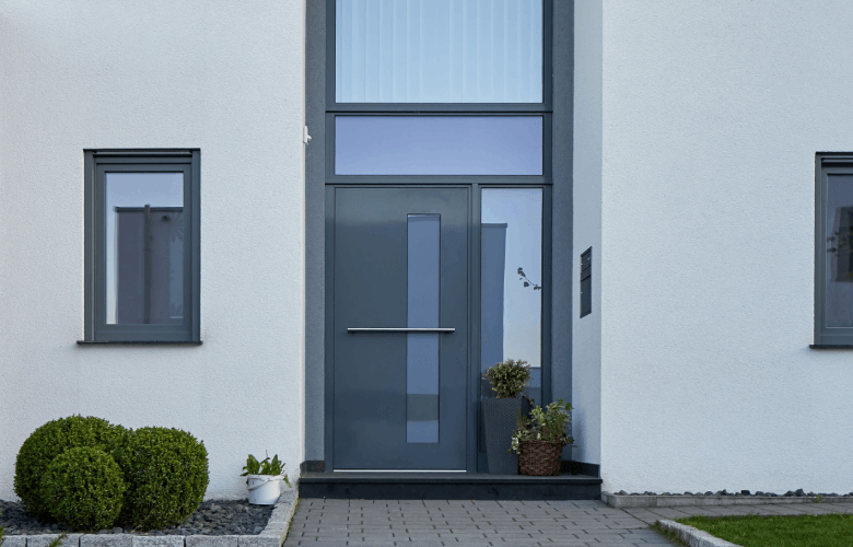 Grijze aluminium buitendeur met glazen elementen in een witte voorgevel.