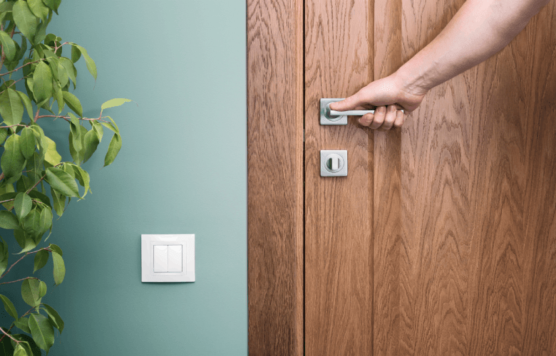 Een hand opent een houten binnendeur in een groene muur.